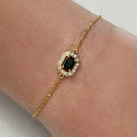 Gold gemstone bracelet with emerald green stone in ornate rectangular frame