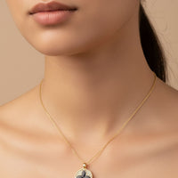 Gold necklace close-up: round clover pendant with black enamel center on chain