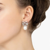 Silver pearl drop earrings with bow ribbon detail, worn close-up on ear