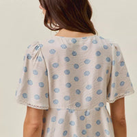 Back view of ivory dot-print blouse with gathered flutter sleeves and tiered waist.