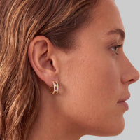 Gold-tone rainbow baguette huggie earrings on ear, shown in side profile