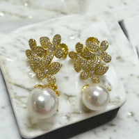 Gold rhinestone floral earrings with white pearl drops on jewelry tray