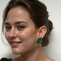 Large emerald-green flower stud earrings on model, gold-tone posts