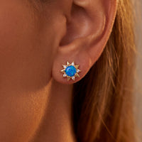 Gold sunflower blue opal stud earrings on ear with starburst crystal setting