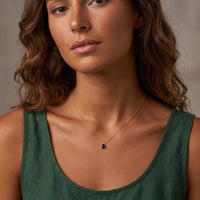 Gold teardrop necklace with blue gemstone pendant worn at neckline