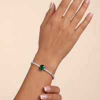 Silver tennis bracelet on wrist with emerald green oval center gemstone and white stones