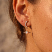 Gold crescent moon and white opal starburst drop earrings on ear with hinged backing