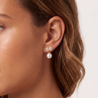 Gold-tone pearl drop earrings with crystal flower tops, worn on ear