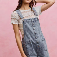 Light wash denim overall romper with adjustable straps, button front, and patch pockets