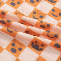 Close-up texture of orange-and-white checkered fabric with jack-o’-lantern faces