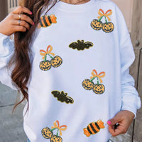 White sequin pullover sweatshirt with jack-o'-lantern, bat, and candy corn motifs