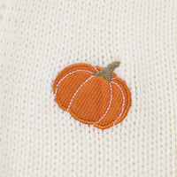Close-up of orange pumpkin embroidery on off-white knit cardigan fabric.