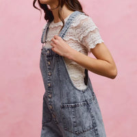 Light wash denim overall romper with adjustable straps and front button placket, side pockets