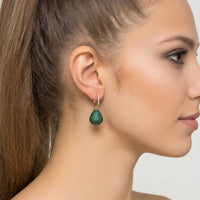 Emerald-green teardrop gemstone drop earring on gold hook, close side view