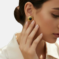 Gold spiral round onyx stud earrings on the ear.
