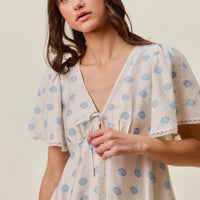 Ivory blouse with blue dot pattern, tie-front V-neck, and short flutter sleeves.