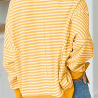 Back view of gold-and-white striped long-sleeve top with orange split-hem detail