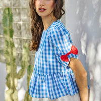 Blue gingham short-sleeve peplum blouse with red shoulder ribbon bows and gathered hem