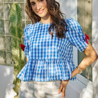 Blue gingham peplum blouse with short puff sleeves and red bow ties on both shoulders