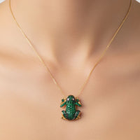 Gold frog pendant necklace worn on chest; green and blue-toned enamel