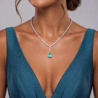 Silver crystal necklace with turquoise teardrop pendant, worn on a deep teal dress