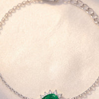 Close-up silver bracelet with emerald-green oval gemstone and starburst crystals