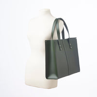 Green leather tote bag on dress form, with top handles and snap detailing