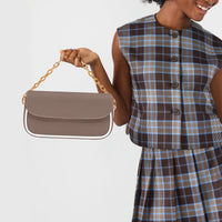 Brown leather shoulder bag with front flap and gold chain strap, held by hand
