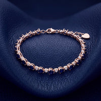 Gold-tone tennis bracelet with blue faceted stones and heart-shaped clasp charm