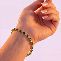 Rose gold tennis bracelet with green heart stones, shown on an extended wrist