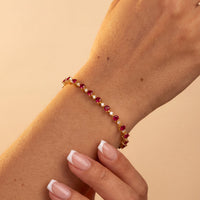 Gold-tone heart tennis bracelet with ruby-pink heart stones on forearm
