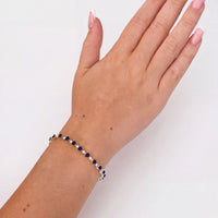 Silver tennis bracelet with blue heart-cut gemstones on raised hand