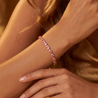 Gold-tone heart-stone tennis bracelet on wrist with pink ruby hearts in links