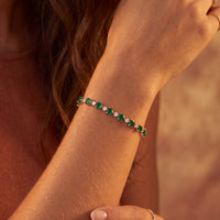 Rose gold tennis bracelet with green emerald-cut heart stones on the wrist