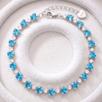 Silver heart-cut blue topaz tennis bracelet on white jewelry cushion