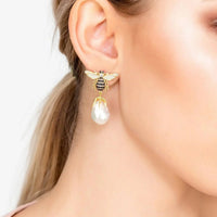 Gold-tone bee earrings with crystal wings and white pearl drop, worn on ear