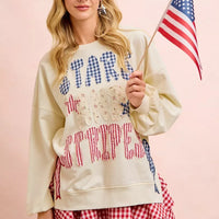 Cream sweatshirt with star-and-stripe patch graphic and red-blue bow detail on sleeve.