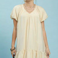 Cream mini shift dress with V-neck and ruffle hem, short puff sleeves.