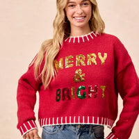 Red crewneck knit sweater with sequin “Merry & Bright” text and striped rib edges