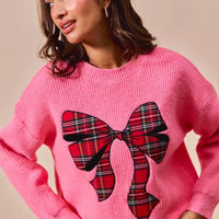 Pink knit Christmas sweater with oversized plaid bow graphic on front