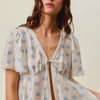 Ivory dot-print blouse with tie-front V-neck and flowing flutter sleeves.