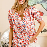 Orange floral V-neck top with gathered puff sleeves and smocked detail, ruffled hem
