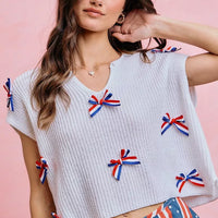 Off-white dolman sweater top with red, white, and blue bow appliques across the chest