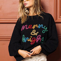 Black sweater with multicolor tinsel "Merry & bright" lettering, crewneck front detail.