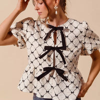 Ivory woven peplum top with black bow tie at neckline and puff sleeves, side view.