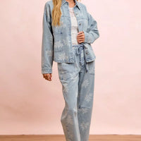 Washed light blue denim jacket with white floral print, worn with matching pants