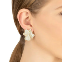 Gold flower stud earrings on model's ear with glittery texture