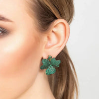 Flower stud earrings with emerald green stones and gold-toned posts worn on ear