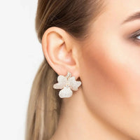 Large four-petal flower stud earrings in rose-gold tone on a modelβs ear