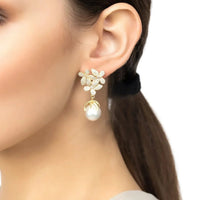 Gold floral earrings with white pearl drop, worn on modelβs ear